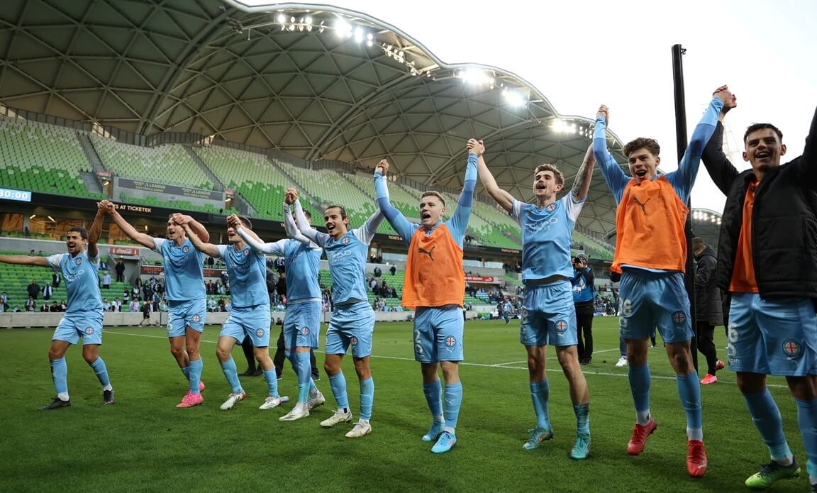 Die Spieler von Melbourne City feiern gemeinsam den Finaleinzug. Sie stehen dabei Hand in Hand nebeneinander und machen offensichtlich die "Welle" mit dem Fanblock.