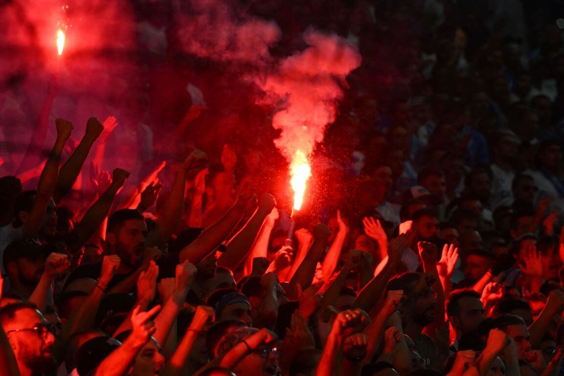 Fans von Olympique Marseille, zwei halten eine brennende rote Fackel hoch.