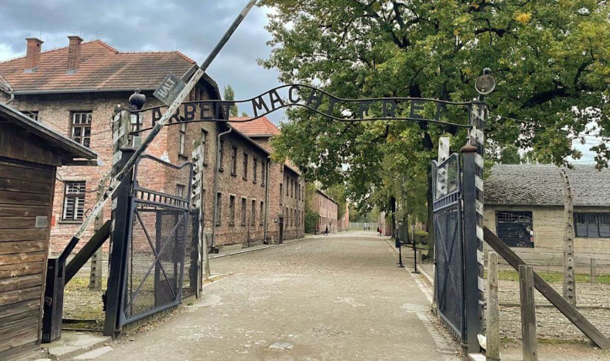 Das Eingangstor mit der Aufschrift" Arbeit macht frei" über dem Eingang. Im Hintergrund die Klinkergebäude des Konzentrationslagers.