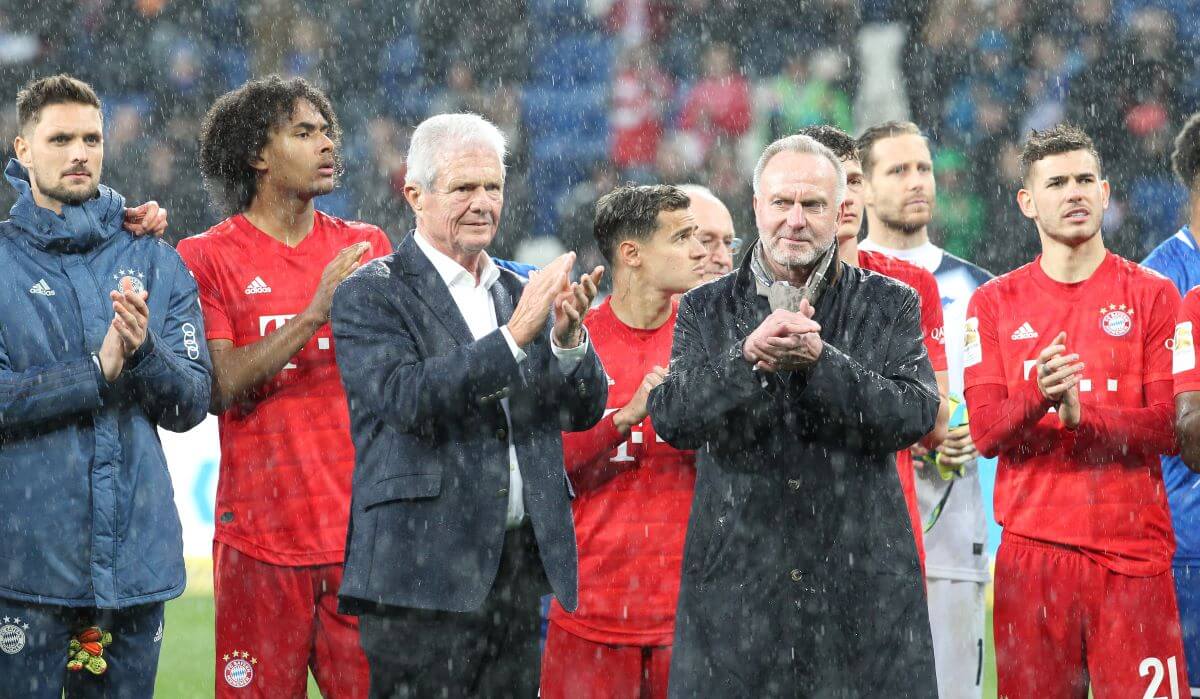 Dietmar Hopp, Karl-Heinz Rummenigge und ein paar Spieler des FC Bayern stehen im Regen.