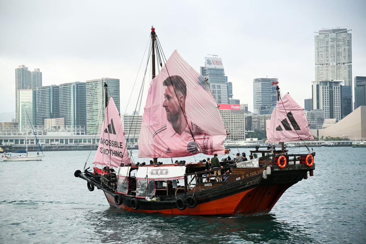 Adidas-Schiff vor der Skyline von Hongkong. Neben rosa Adidas-Logos ist auch ein überdimensionales rosa Segel mit Messi-Foto gespannt.