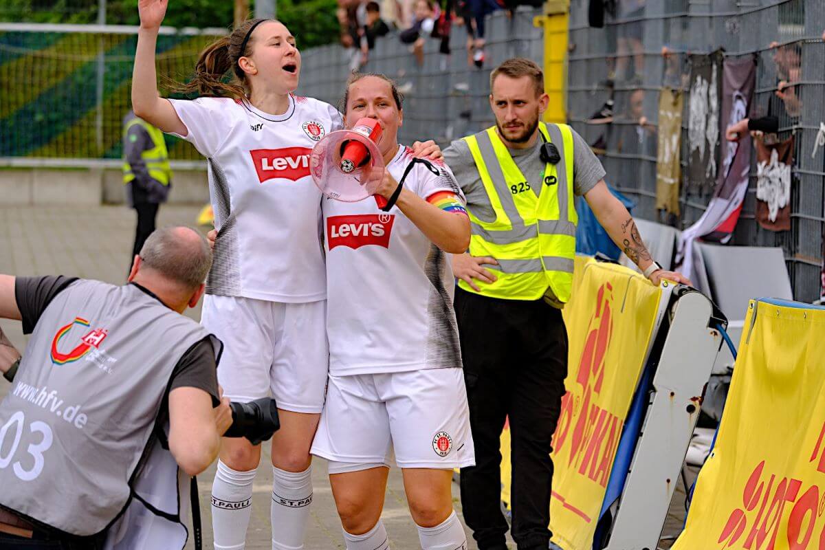 Julia Hechtenberg und Vanessa Zawada nach dem Pokalsieg der 1. Frauen des FC St. Pauli vorm Fanblock, mit Megaphon. 