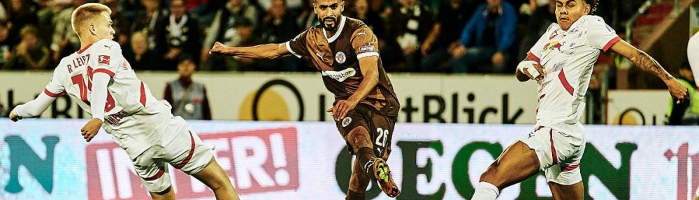 Elias Saad spielt den Ball zwischen zwei Spielern von RB Leipzig hindurch nach vorne.