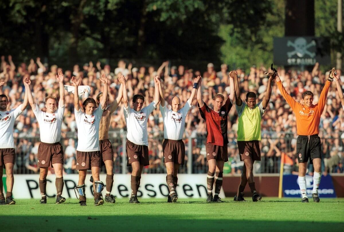 Die Spieler des FC St. Pauli bejubeln nach dem 1. Spieltag der Saison 2001/02 das 0:0 gegen Hertha BSC mit ihren Fans. Von links: Nico Patschinski, Oliver Held, Henning Bürger, Ugur Inceman, Thomas Meggle, Toralf Konetzke, Daniel Scheinhardt, Adamu Yakubu und Tihomir Bulat. // (c) IMAGO / Contrast via OneFootball 