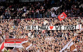 Fans des FC St. Pauli halten auf der Gegengeraden ein Banner mit der Aufschrift "In St. Pauli We Trust" hoch.