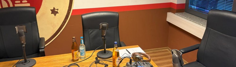 Tisch mit Podcast-Aufnahme-Equipment, im Hintergrund das Vereinslogo des FC St. Pauli