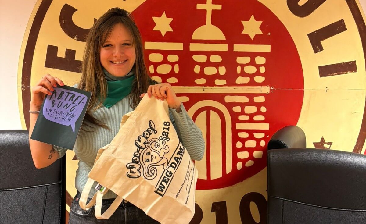 Debbie mit einem "Abtreibungen entkriminalisieren"-Flyer und einem Beutel, der §218 wegkicken will.