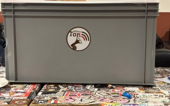 Technikbox mit MillernTon-Logo auf einem wild beklebten Tisch im Fanladen.