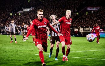 Im Vordergrund zwei Spieler des SC Freiburg in der Vorwärtsbewegung, im Hintergrund ein verzweifelter Jackson Irvine.