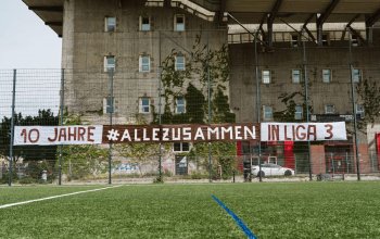 Ein Banner mit dem Schriftzug "10 Jahre #allezusammen in Liga 3" hängt am Zaun der "Feldarena".